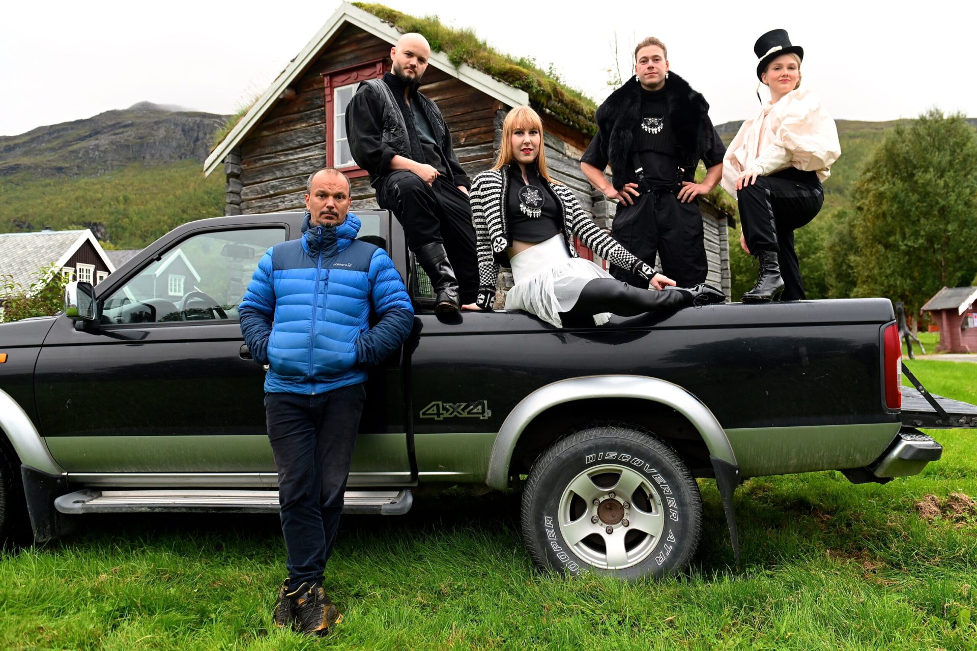 Ensemle og teatersjef poserer på truck foran gammelt hus